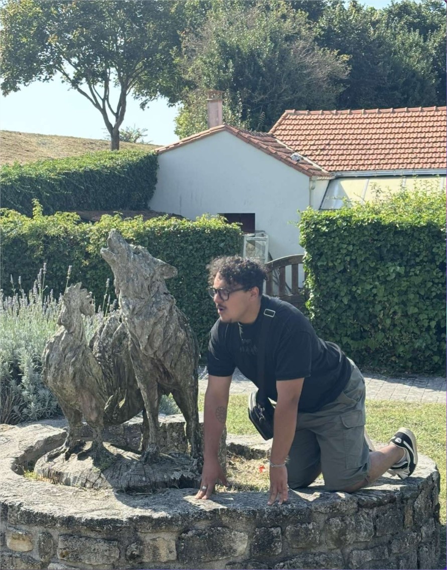 Yanis à quatre pattes sur un muret en pierre imitant un loup à côté d'une statue de loup